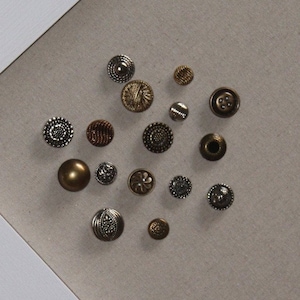 May include: Assortment of metal buttons in various shapes, sizes, and finishes, including silver, gold, and bronze. Some buttons have intricate designs, while others are plain.
