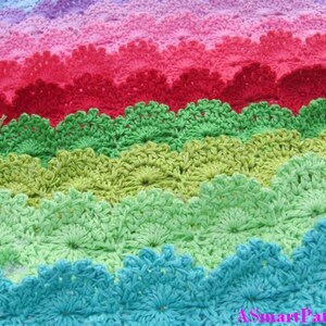 Pode incluir: Uma manta de crochê colorida com uma borda festonada. A manta é feita em tons de azul, verde, rosa e vermelho.
