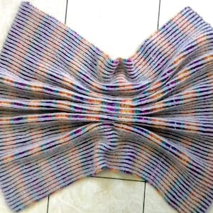 Pode incluir: Uma manta de crochê com um padrão listrado em tons de roxo, cinza, laranja e azul.