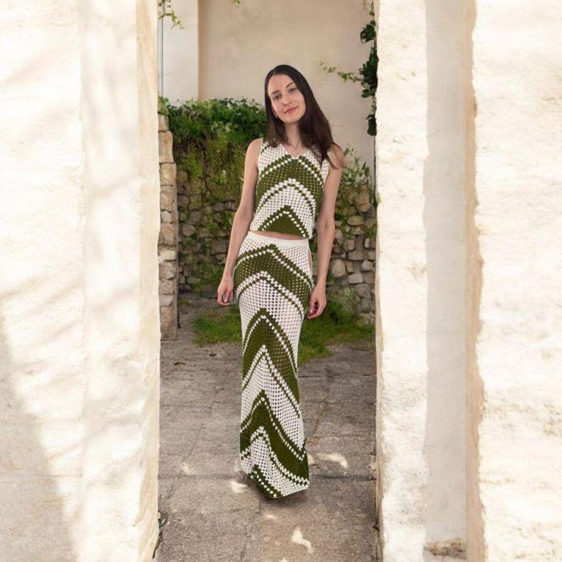 May include: A two-piece crochet outfit in white and olive green. The set includes a sleeveless top and a floor-length skirt with a chevron pattern. The outfit is made of a lightweight, open-weave material, perfect for warm weather.