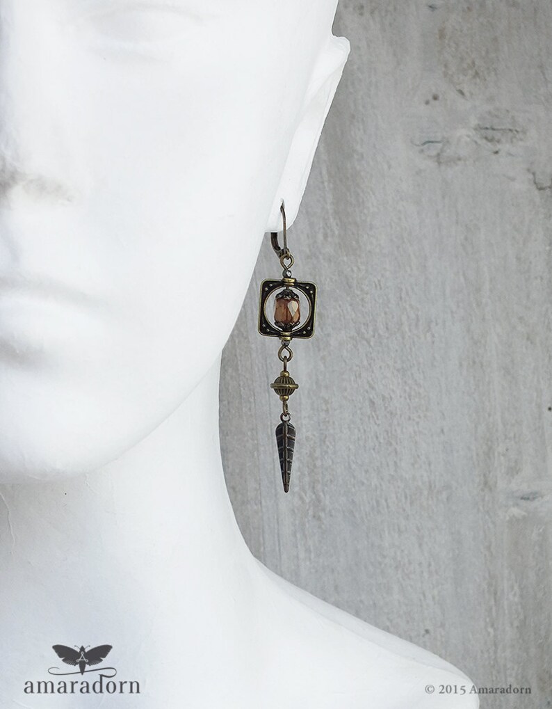 May include: Bronze earrings with a geometric square design featuring a brown faceted gemstone. The earrings dangle with a small round bead and a pointed teardrop shape.