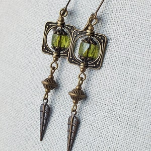 May include: A pair of bronze earrings with green glass beads, square frames, and leaf-shaped accents.