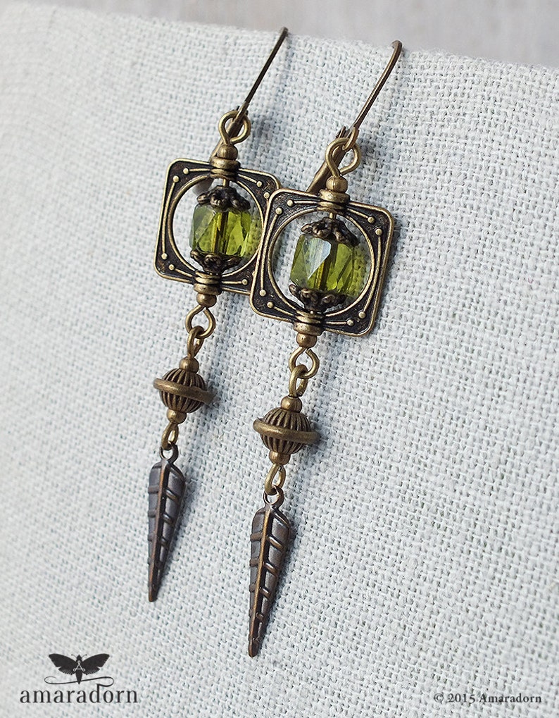 May include: A pair of bronze earrings with green glass beads, square frames, and leaf-shaped accents.