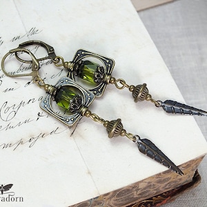 May include: A pair of bronze earrings with green glass beads and a feather design. The earrings are made of metal and have a vintage look.