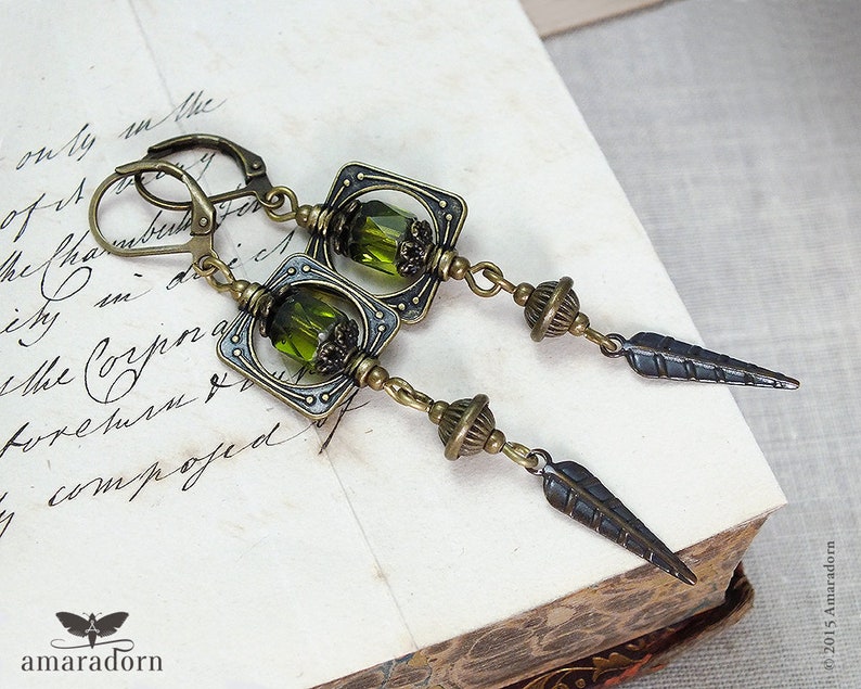 May include: A pair of bronze earrings with green glass beads and a feather design. The earrings are made of metal and have a vintage look.