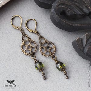 May include: A pair of bronze earrings with a gear design and green glass beads. The earrings are hanging from a hook.