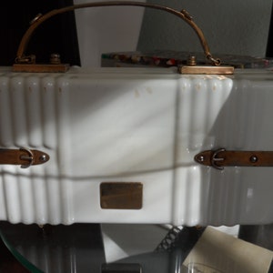 Op de afbeelding: Een witte vintage handtas met een gouden handvat en metalen accenten. De tas heeft een rechthoekige vorm en een licht getextureerd oppervlak.