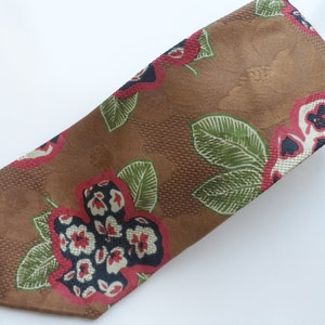 Puede incluir: Una corbata de seda marrón con un estampado floral que presenta flores rojas, blancas y negras sobre un fondo de hojas verdes.