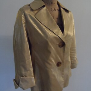 May include: A gold metallic blazer with a notched collar and three buttons. The blazer has long sleeves with cuffed ends.