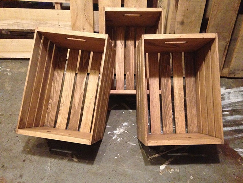 May include: Three wooden crates with a rustic brown finish. The crates have a rectangular shape with open tops and sides. The crates are stacked on top of each other.