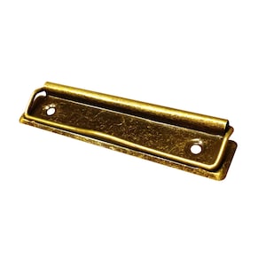 May include: A gold-toned metal binder clip with a textured finish. The clip has two holes on the top and a curved lip on the bottom.