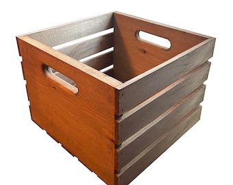May include: A wooden crate with a rectangular shape and a natural wood finish. The crate has a slatted design on the sides and features cut-out handles on each end. The interior is visible, and the wood grain adds texture.