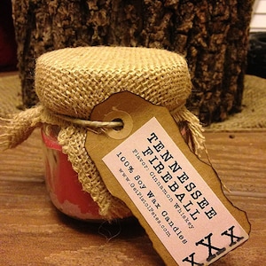 May include: A brown burlap-wrapped candle jar with a label that reads "Tennessee Fireball" and "Flavor: Cinnamon Whiskey 100% Soy Wax Candles www.GetPistolPets.com".