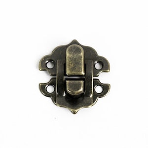 May include: Antique brass latch with a decorative design. The latch has two holes on each side for attaching to a surface.