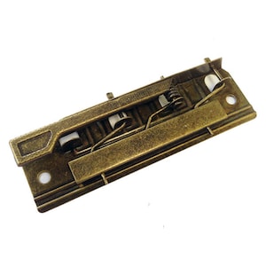 May include: A brass binder clip with a spring mechanism. The clip is closed and ready to hold papers.