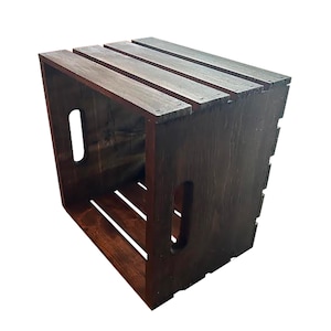 May include: A dark brown wooden crate with a rectangular shape. The crate has a slatted top and sides, with cut-out handles on the sides. The wood grain is visible, and the crate appears to be stained or painted.
