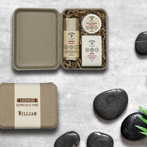 May include: A brown cardboard box with a white label that says "HAND-MADE (ESPECIALLY FOR) WILLIAM". The box is open and contains a set of three natural bath and body products: a deodorant stick, a solid cologne, and a bar of soap. The products are all packaged in brown paper with white text.