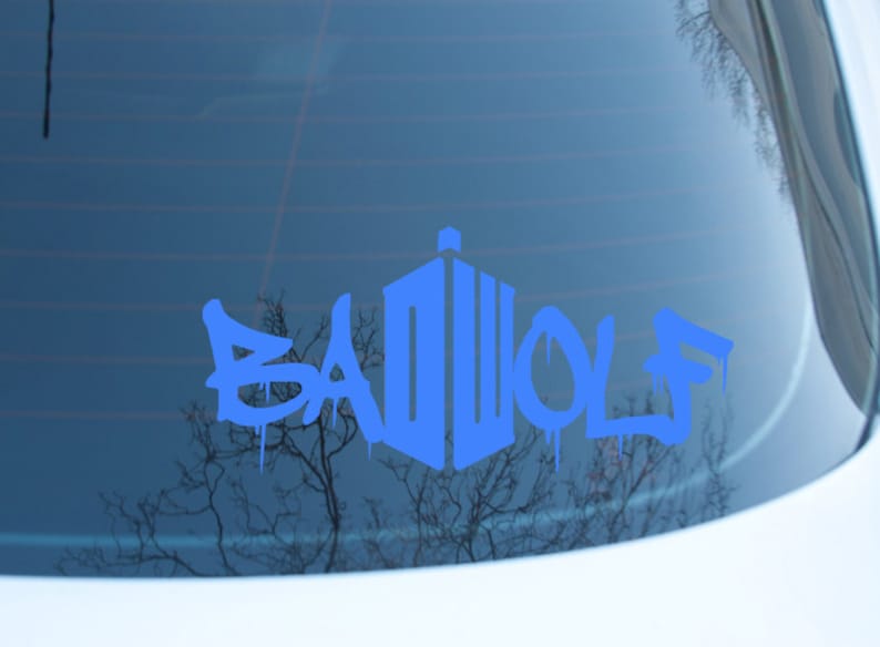 May include: Blue vinyl decal featuring the text "BAD WOLF" in a graffiti-style font, with a stylized police box design. The decal is applied to a car window, with a blurred background.