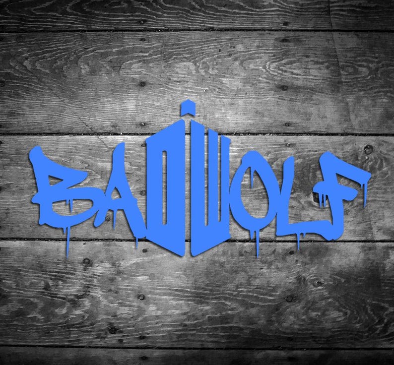 May include: Blue graffiti-style text on a wooden background. The text reads "BAD WOLF" with a stylized design resembling a police box. The background is a grayscale wood grain pattern.