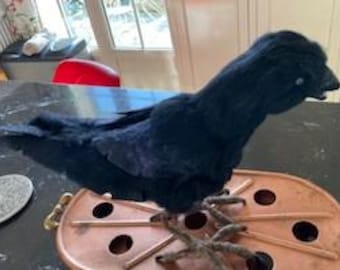May include: A black crow figurine with realistic feathers and a detailed beak. The crow is perched on a copper stand with a decorative design.