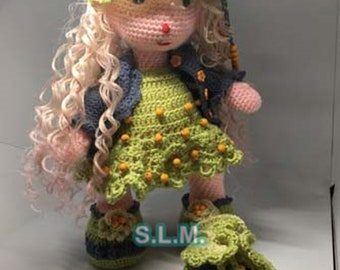May include: A crocheted doll with long blonde curly hair, wearing a blue and green hat, a green dress with yellow beads, and blue shoes with green accents. The doll is holding a green and yellow crocheted bag with yellow beads.