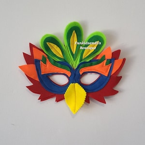 May include: A colorful felt mask with a layered design. The mask features a blue base with orange, green, and red accents. A yellow leaf shape is at the bottom. The text "FunkidsandUs Boutique" is visible.