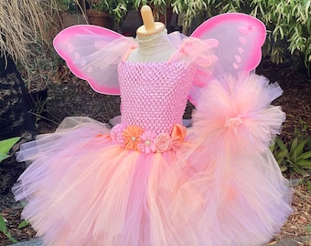 May include: A pink and orange tulle tutu with a pink crocheted bodice and matching butterfly wings. The tutu has a flower sash with orange, pink, and white flowers.