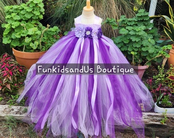May include: A purple and white tulle tutu dress with a flower embellishment on the bodice. The dress has a satin ribbon sash and is displayed on a mannequin.