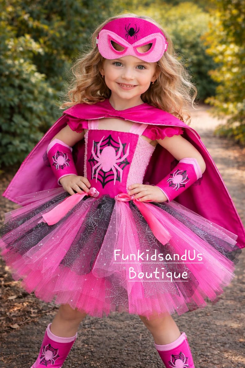 Op de afbeelding: Een roze superhelden kostuum met een masker, cape en tutu rok. Het kostuum heeft een spinnenweb ontwerp en een groot spinnen embleem op het lijfje. De outfit bevat bijpassende armmanchetten en laarzen, perfect voor verkleden en fantasierijk spel.