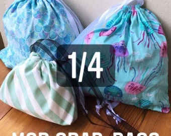 May include: Four drawstring bags with different patterns, including a mermaid scale pattern, a jellyfish pattern, and a striped pattern. The bags are arranged on a wooden surface. The text "1/4" is visible in the center of the image. The text "MSD Grab-Bags Mystery Bag" is visible at the bottom of the image.