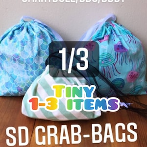 Könnte beinhalten: Drei Kordelbeutel mit verschiedenen Mustern. Die Beutel sind mit "1/3 TINY 1-3 ITEMS SD GRAB-BAGS MYSTERY BAGS" beschriftet.