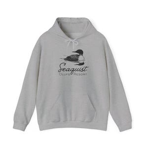May include: A light gray hooded sweatshirt with a front pocket and drawstring. The front features a black and white illustration of a loon on water, with the text "Seaquist Olufs Resort" below the image.