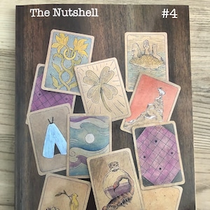 May include: The Nutshell #4, a comic book by Brandon Thomas Olterman, features a collection of illustrated cards with various images, including a four-leaf clover, a scorpion in a bottle, and a bird in a nest.