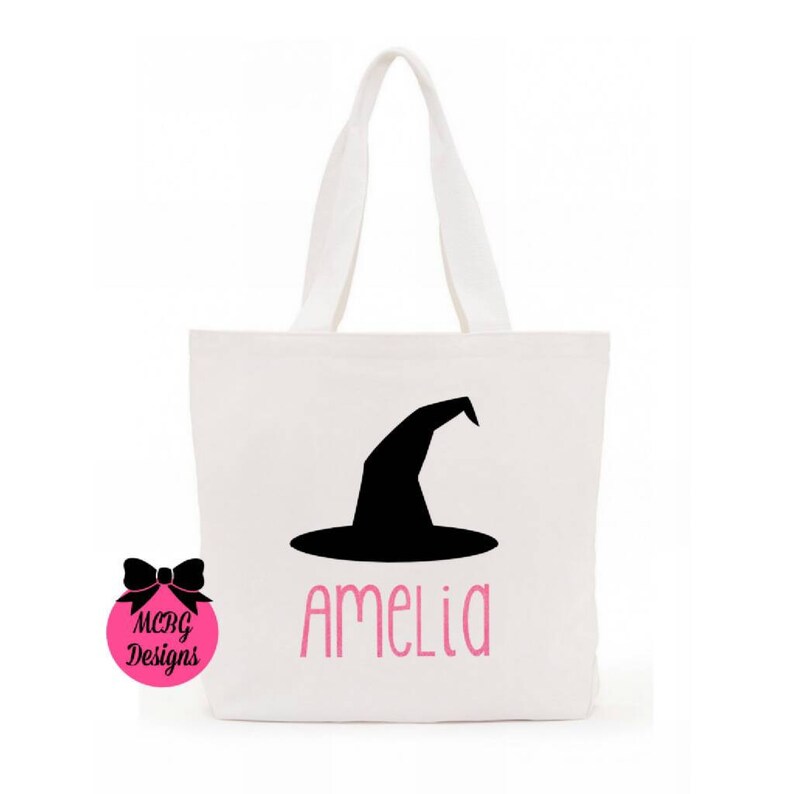 May include: White canvas tote bag with a black witch hat and the name Amelia printed in pink.