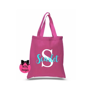 May include: A pink canvas tote bag with a white letter "S" and the word "Scarlet" in turquoise lettering.