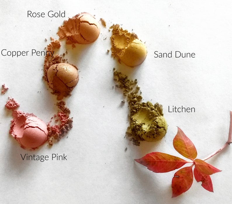 May include: Five small samples of loose eyeshadow powder in various shades of pink, orange, yellow, and green. The colours are labelled "Rose Gold", "Copper Penny", "Sand Dune", "Vintage Pink", and "Litchen".