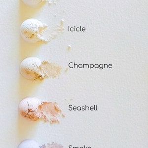 May include: Five small round containers of loose powder makeup in shades of white, ivory, beige, light peach, and grey. The shades are labelled "White Witch", "Icicle", "Champagne", "Seashell", and "Smoke".