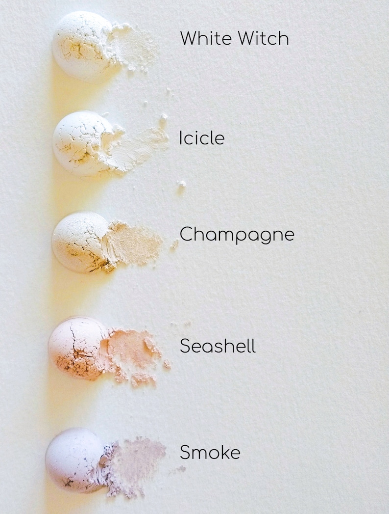 May include: Five small round containers of loose powder makeup in shades of white, ivory, beige, light peach, and grey. The shades are labelled "White Witch", "Icicle", "Champagne", "Seashell", and "Smoke".