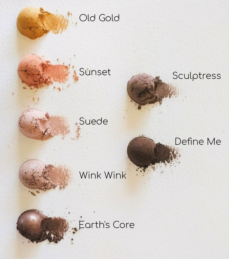 May include: Six eyeshadows in various shades of brown, pink, and gold. The eyeshadows are arranged in a vertical line from top to bottom. The names of the eyeshadows are written below each one: Old Gold, Sunset, Sculptress, Suede, Wink Wink, and Earth's Core.
