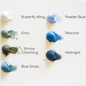 May include: Eight small round containers of blue, green, and white powder pigments. The containers are labelled with the names "Butterfly Wing", "Powder Blue", "Envy", "Peacock", "Prince Charming", "Midnight", "Blue Grass", and "White".