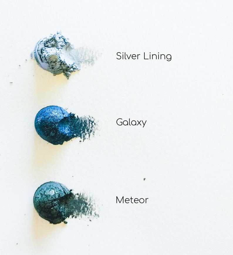 May include: Three eyeshadow samples in shades of blue and grey. The samples are labelled "Silver Lining", "Galaxy", and "Meteor".