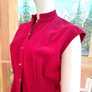 May include: A red sleeveless blouse with a mandarin collar and gold buttons. The blouse has a slightly fitted silhouette.