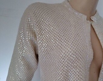 May include: A cream-colored cardigan with a sparkly, beaded texture. The cardigan has a button-up front and short sleeves.
