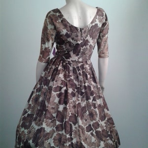 May include: A brown and white floral print dress with a scoop neckline and 3/4 sleeves. The dress has a fitted bodice and a full skirt.