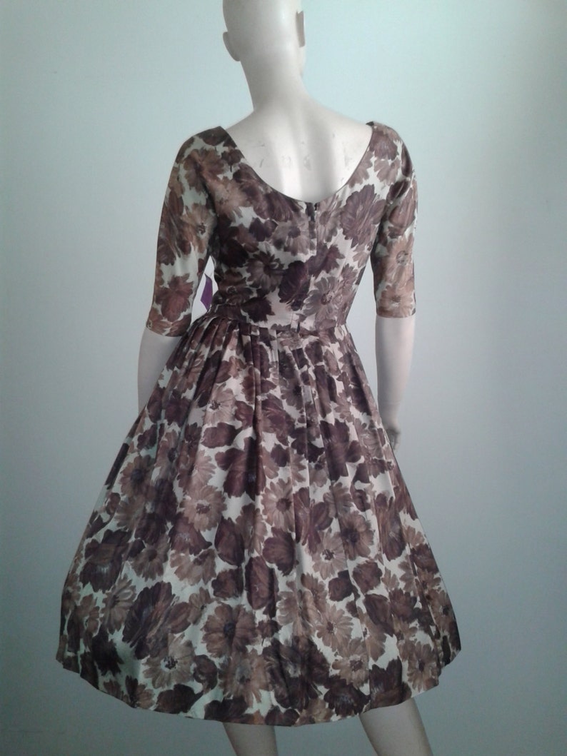 May include: A brown and white floral print dress with a scoop neckline and 3/4 sleeves. The dress has a fitted bodice and a full skirt.