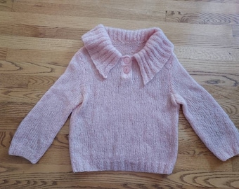 May include: A pink knitted sweater with a large, fluffy collar and two buttons. The sweater is made of a soft, fuzzy yarn.
