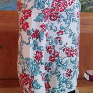 May include: White cardigan sweater with a floral pattern in red and teal. The sweater features a crew neck and long sleeves. The floral design includes stylized flowers and scrolling vines. The sweater is shown on a mannequin.