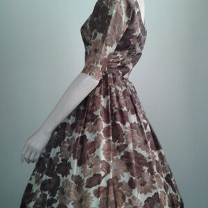 May include: A brown and white floral print dress with a fitted bodice and a full skirt. The dress has a scoop neckline and short sleeves.