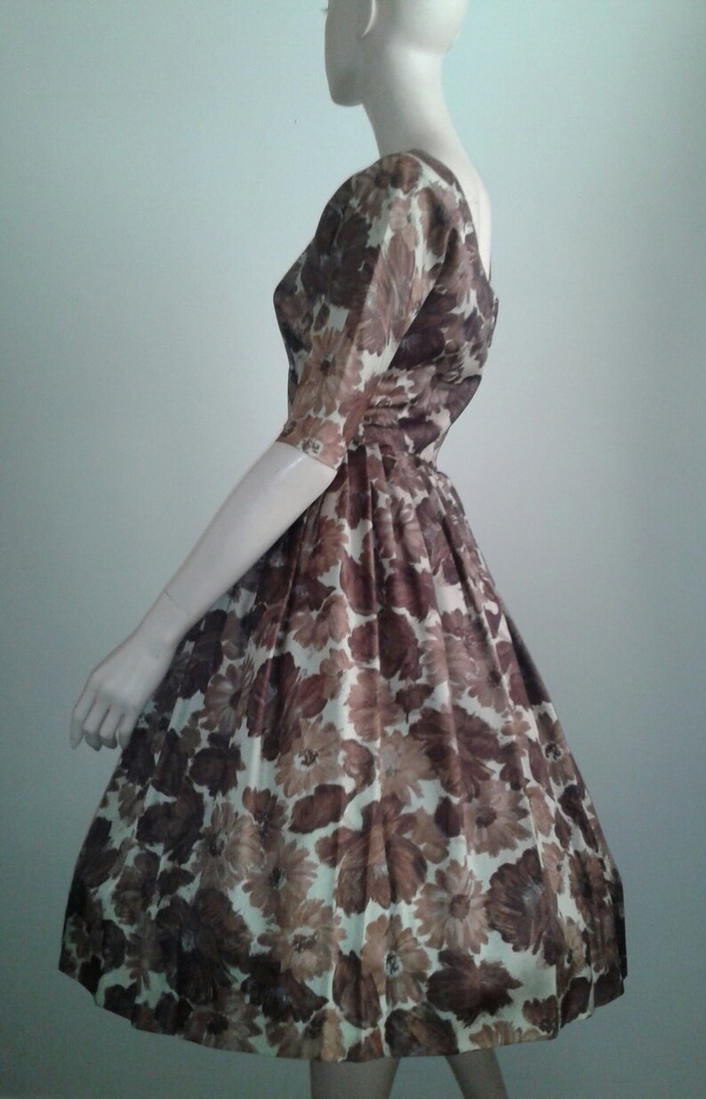 May include: A brown and white floral print dress with a fitted bodice and a full skirt. The dress has a scoop neckline and short sleeves.