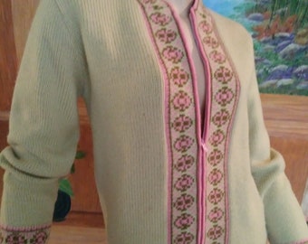 May include: A light green zip-up cardigan with a pink and brown geometric pattern along the zipper, collar, and cuffs. The sweater has long sleeves and a ribbed knit texture. The zipper is pink.